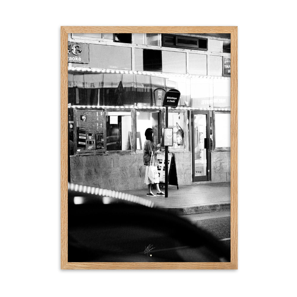 Photographie en noir et blanc d'une femme éclairée par son téléphone dans une rue sombre, mettant en évidence le contraste lumineux de la scène urbaine.