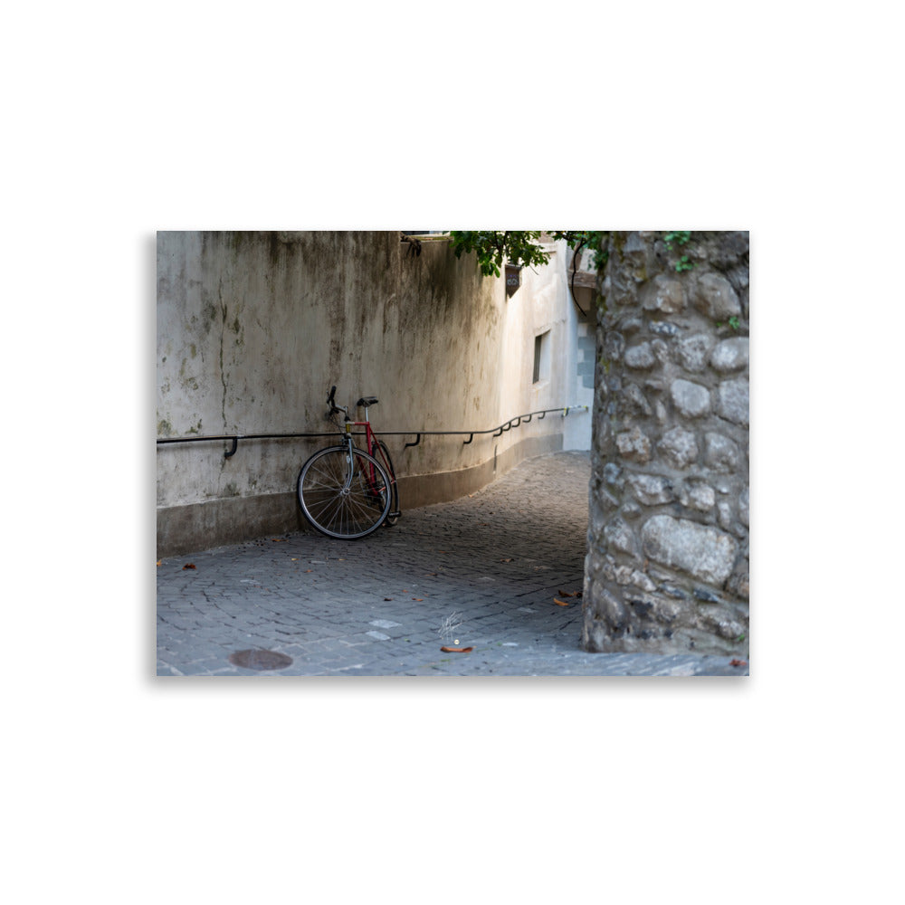 Photographie d'une rue pavée en descente de Genève, sans voitures, avec un vélo non attaché au premier plan. L'atmosphère est paisible et le coucher de soleil ajoute une teinte chaude à la scène.