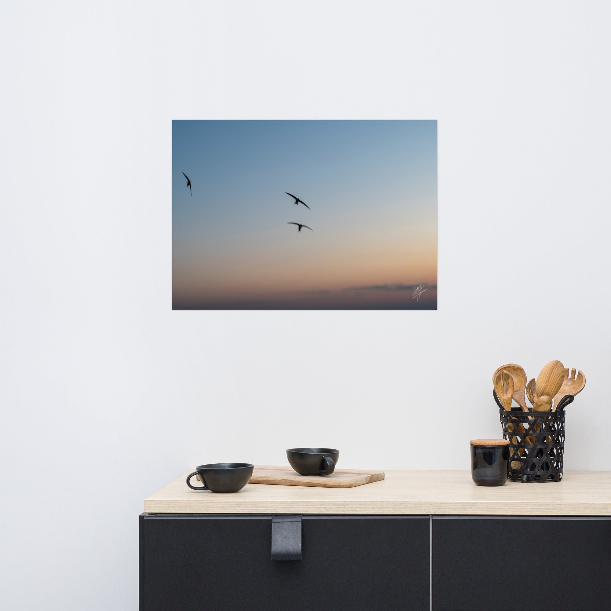 Trois oiseaux volant dans un ciel aux teintes de bleu, orange et jaune.