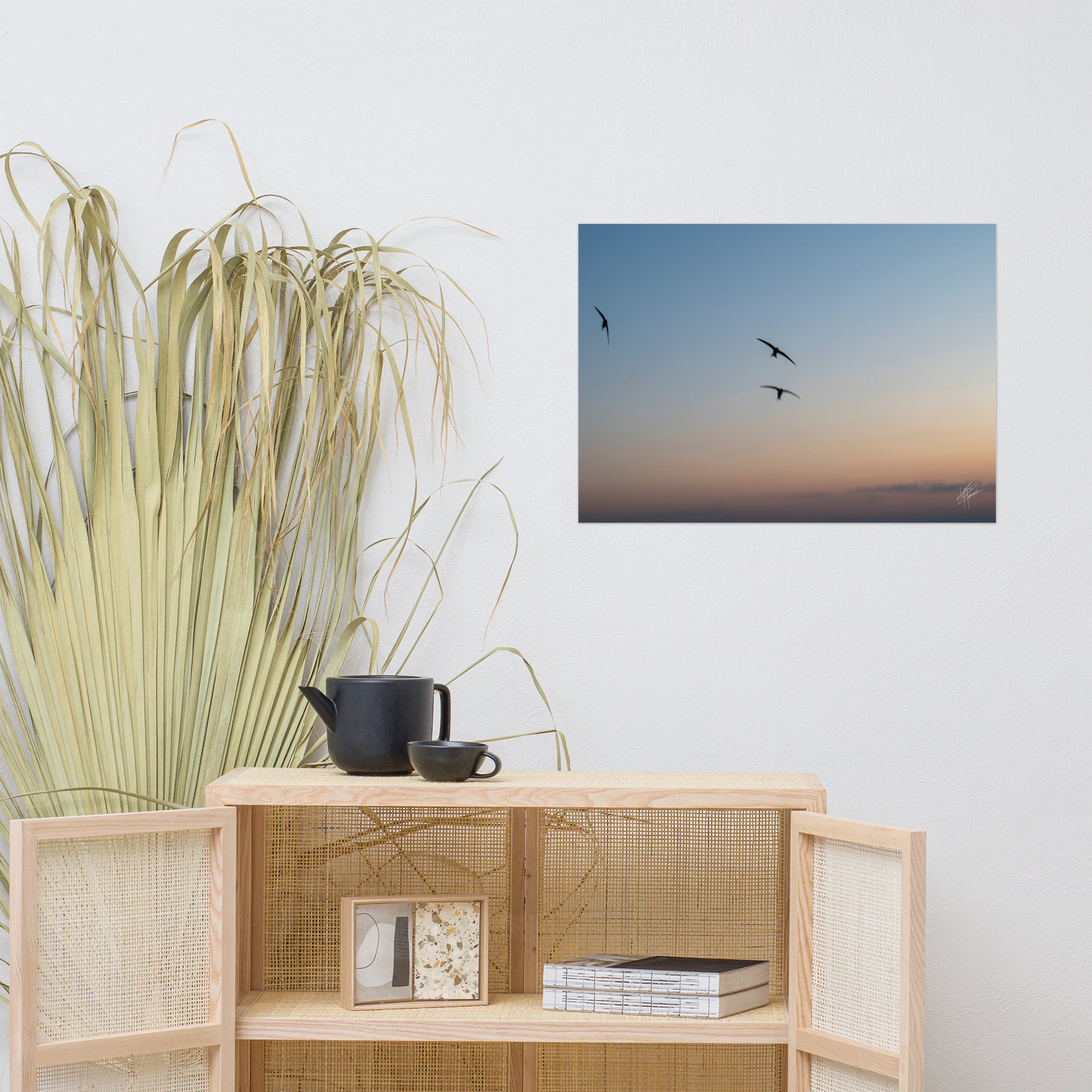 Trois oiseaux volant dans un ciel aux teintes de bleu, orange et jaune.